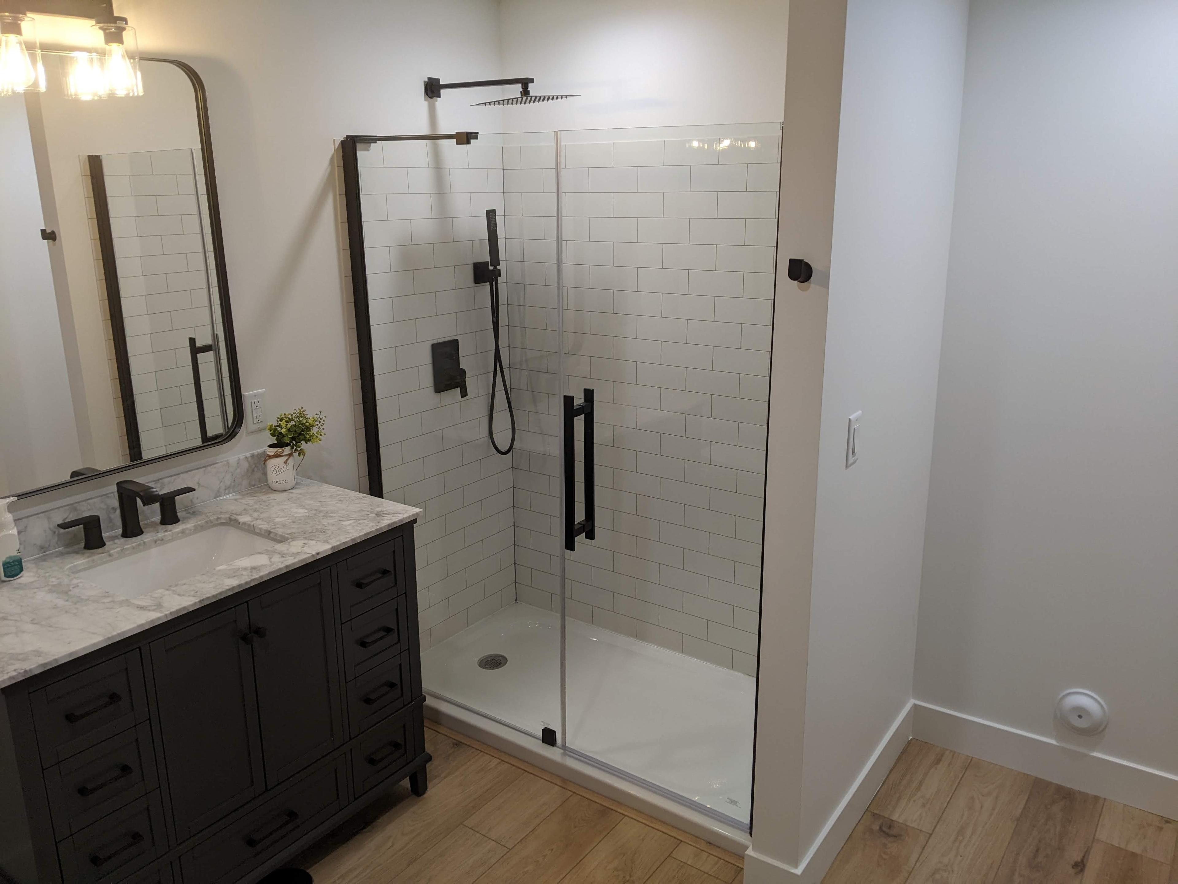 Walk-in tiled shower remodel with matte black fixtures and a glass door
