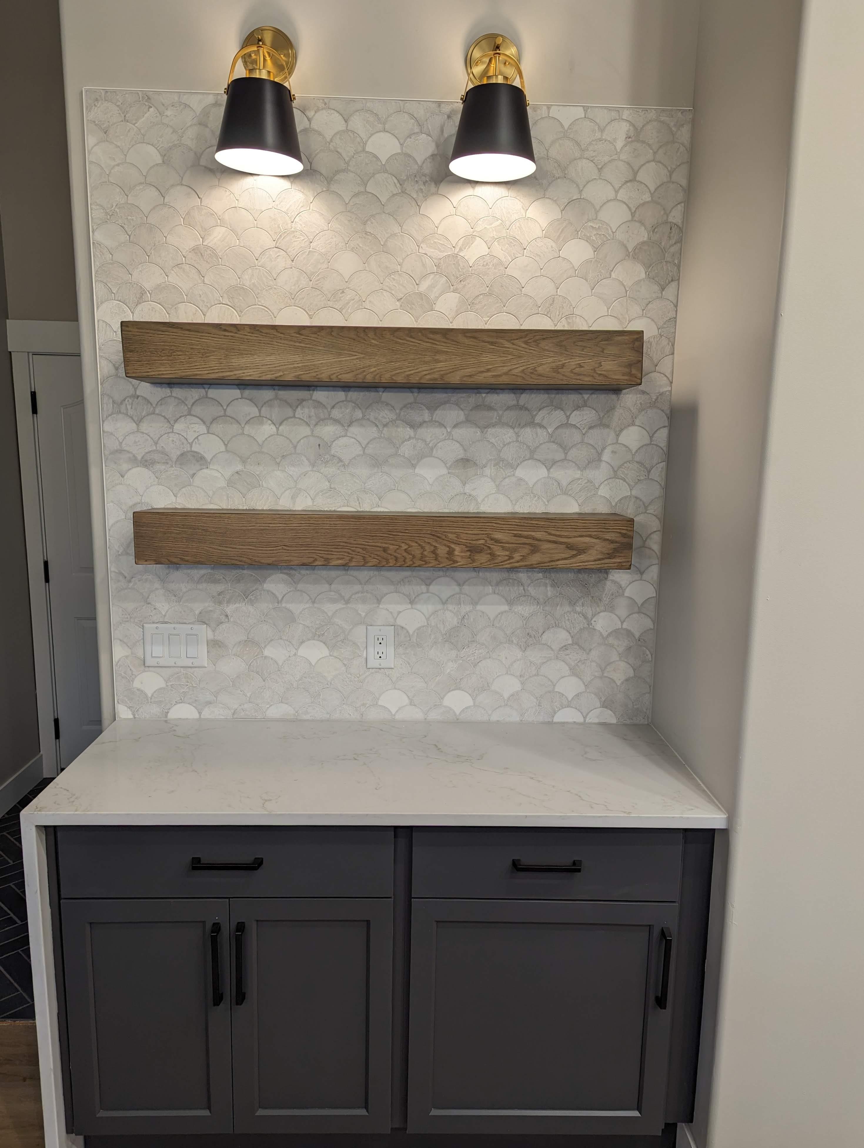 Basement wet bar nook with scalloped tile backsplash, floating wood shelves, and brass sconces