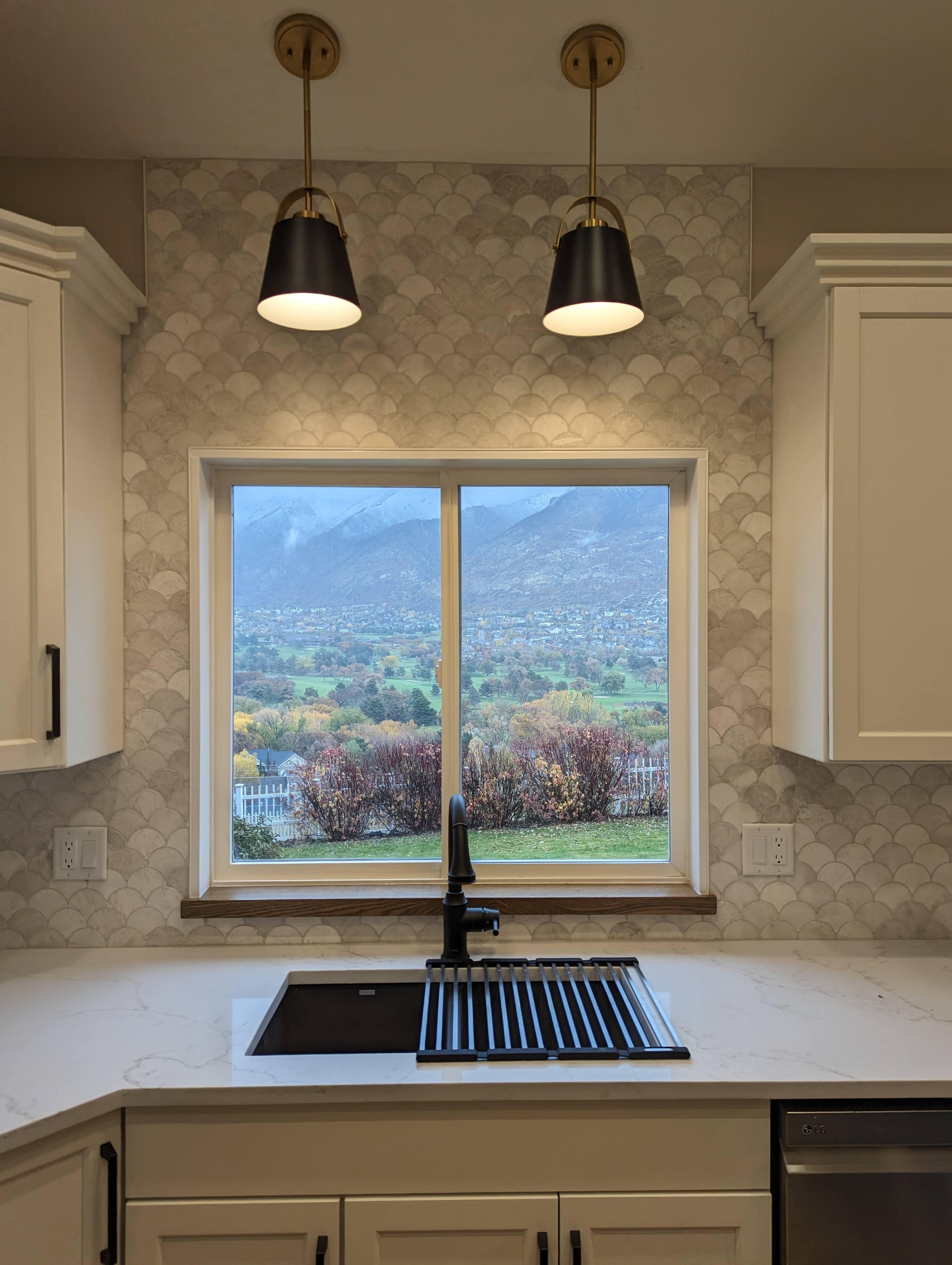 Kitchen sink remodel with scalloped tile backsplash, brass pendant lighting, and a mountain valley view