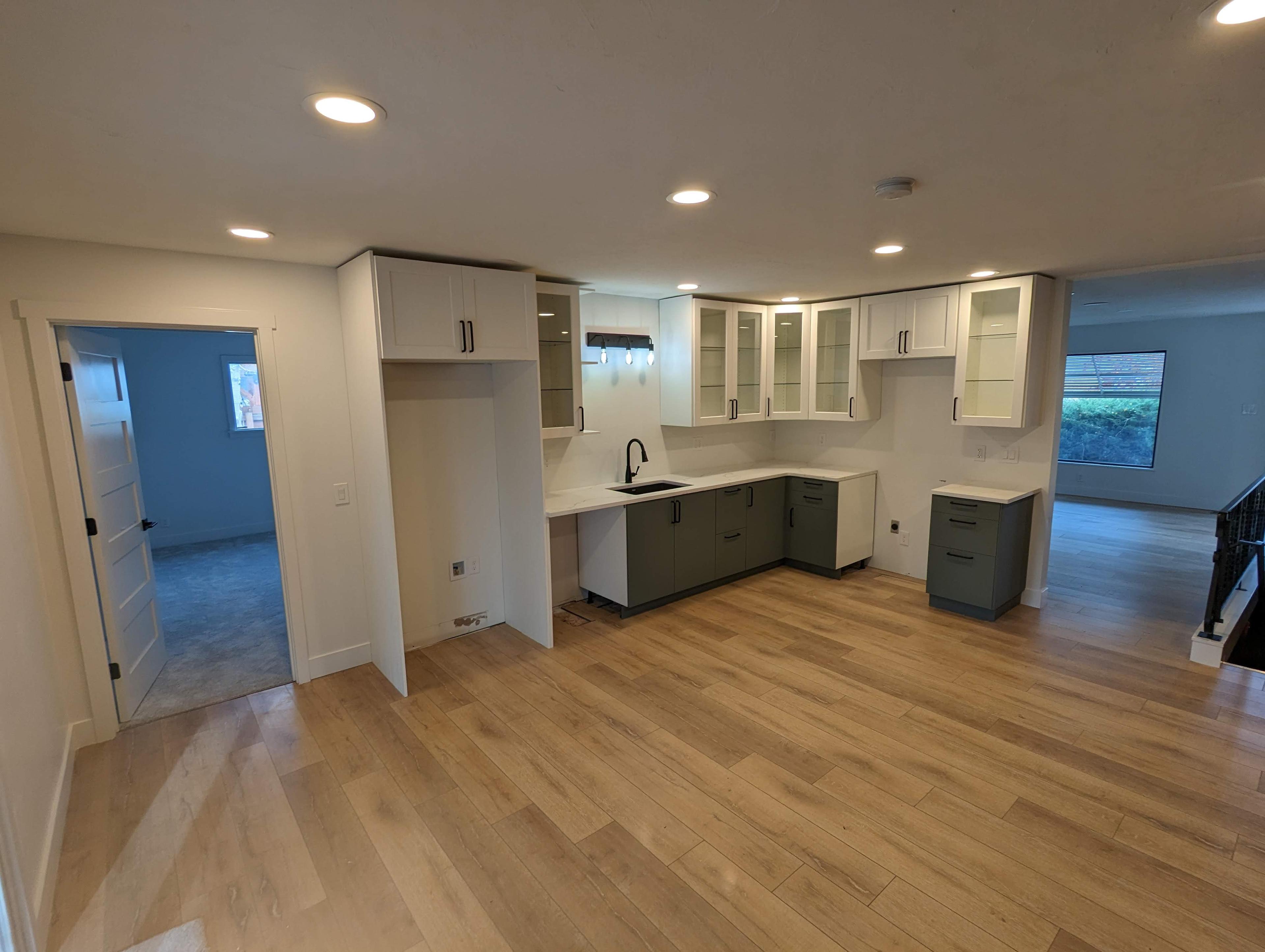 Basement kitchenette remodel with white and sage cabinetry, open to the living area