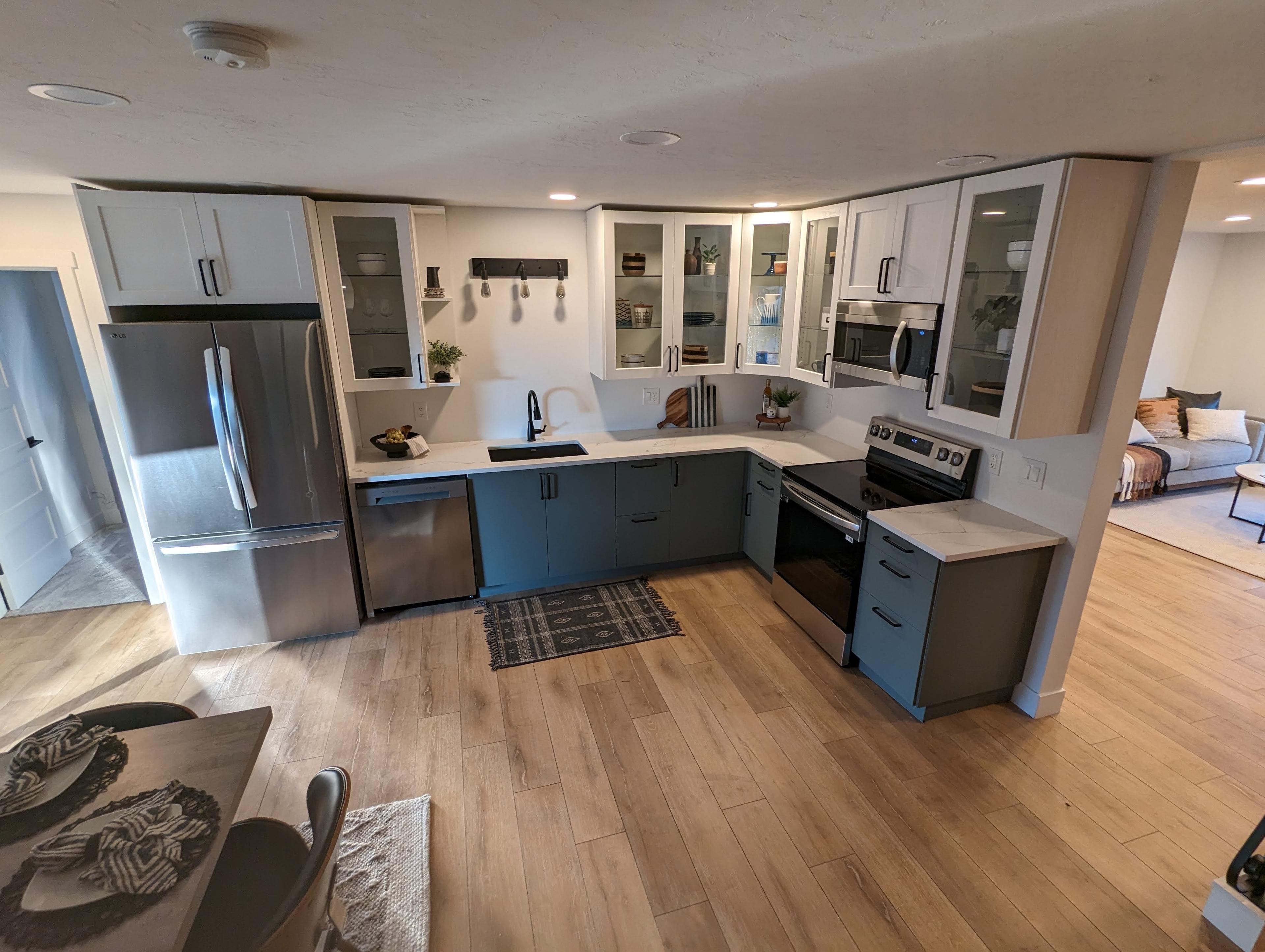 Open-concept kitchen remodel with glass-front white upper cabinets and blue-gray lower cabinets, opening into the living room